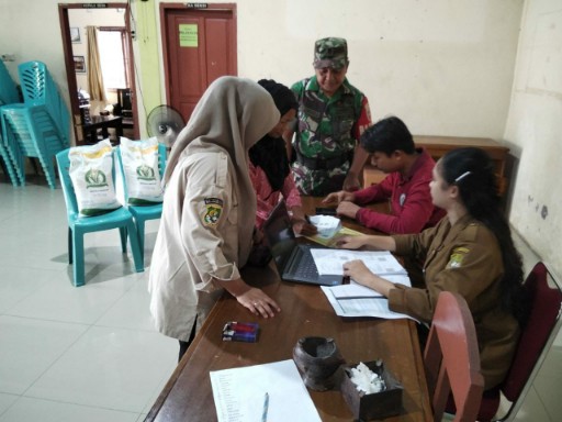 Babinsa Koramil 05/Dua Pitue mendampingi proses administrasi penyaluran bantuan beras di kantor desa bersama aparat dan warga.