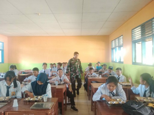 Seorang Babinsa Sidrap mendampingi siswa saat makan makanan bergizi gratis di ruang kelas dalam program penyaluran bantuan gizi di Sidrap.