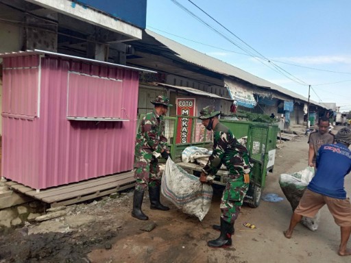 Dua Babinsa Koramil 05/DP mengangkat karung sampah saat kerja bakti bersama warga membersihkan saluran air di Tanru Tedong.