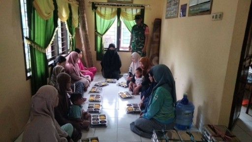 Babinsa dampingi ibu-ibu dan anak saat pembagian makanan bergizi.