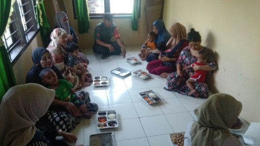 Babinsa dampingi ibu dan anak saat pembagian makan siang bergizi.