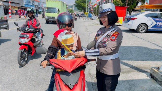Petugas Satlantas Polres Poso membagikan bendera Merah Putih kepada pengendara motor dalam rangka HUT RI ke-80.