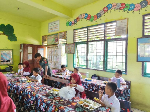 Babinsa mendampingi murid SD saat menikmati makan bergizi gratis di kelas.
