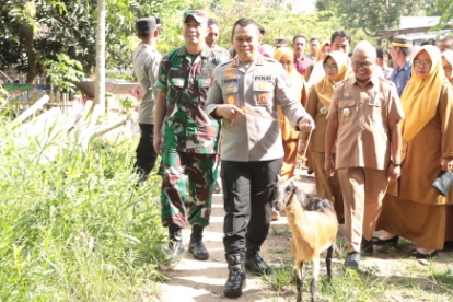 Kapolres Sidrap berjalan bersama Dandim dan rombongan Forkopimcam sambil memegang seekor kambing saat menyerahkan bantuan sosial kepada warga.