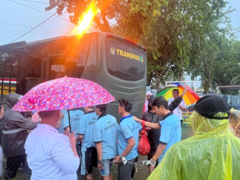 Para petugas mengevakuasi warga binaan dari Rutan Kelas II B Pangkalan Brandan menggunakan bus Transpas di tengah banjir dan hujan lebat, sementara sejumlah orang memegang payung untuk melindungi mereka.