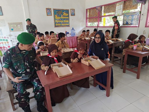 Personel TNI AD bersama guru mendampingi siswa SDN 16 Pangkajene saat menerima dan menikmati makanan dari Program Dapur Satuan di dalam ruang kelas.